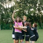 A joyful team celebrates a soccer victory, holding a trophy and embracing on the field.