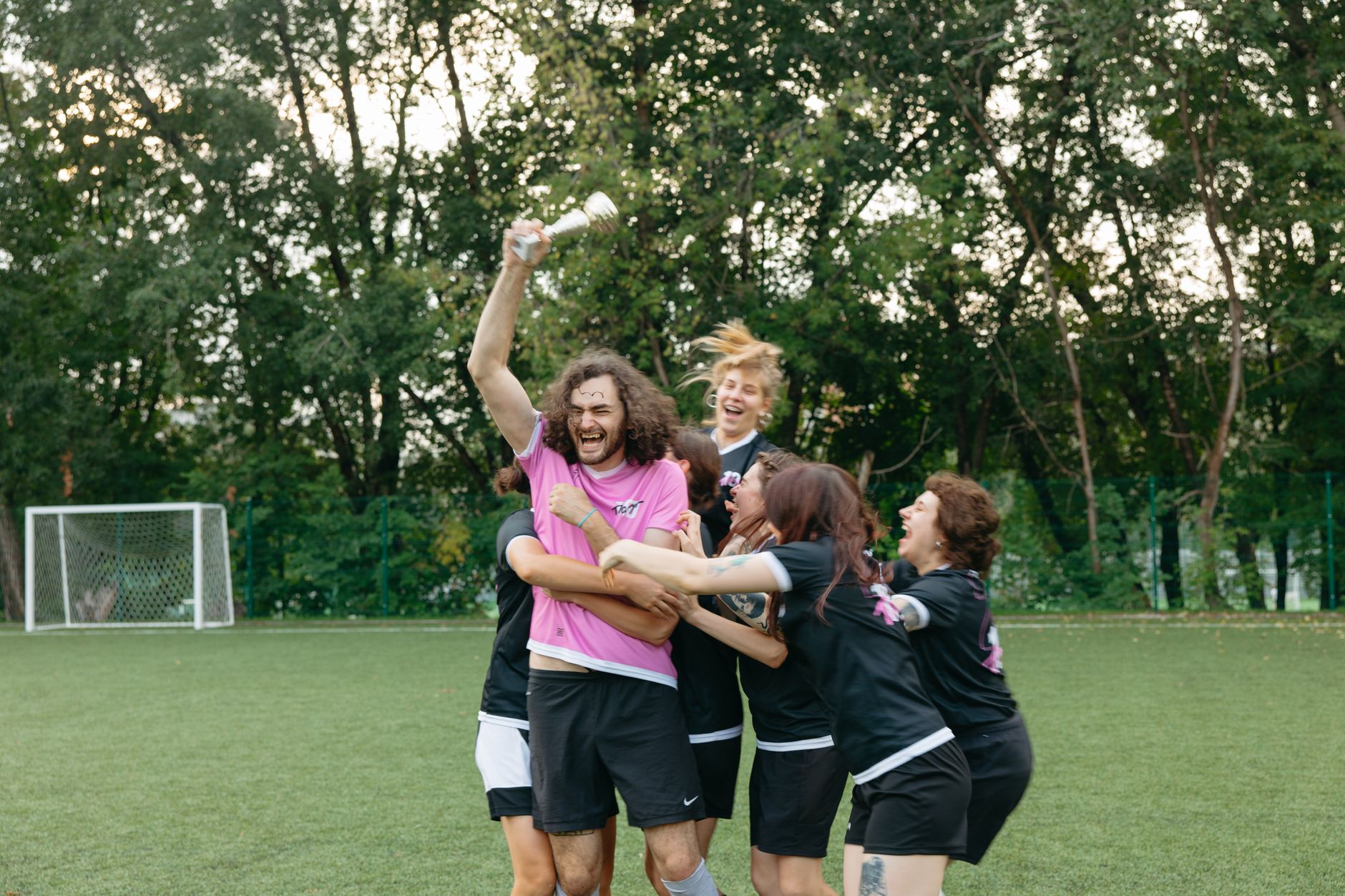 A joyful team celebrates a soccer victory, holding a trophy and embracing on the field.