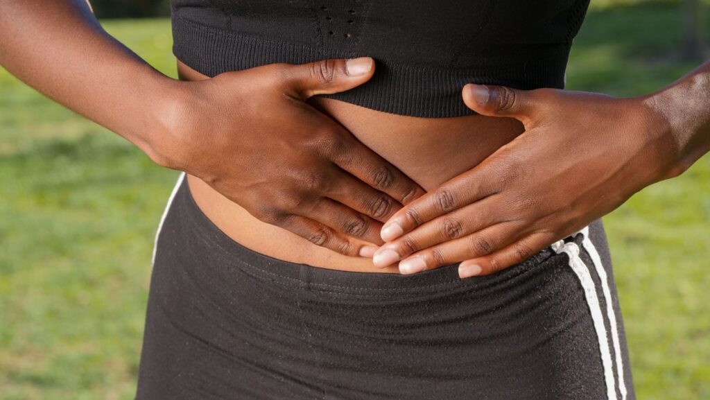 Close-up of a person holding their stomach, indicating abdominal pain outdoors.