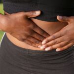Close-up of a person holding their stomach, indicating abdominal pain outdoors.