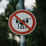 Circular no drone zone sign attached to a pole in a forest with a blurred bokeh background.