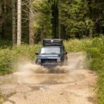 4x4 vehicle splashing through a muddy trail in a dense forest in Asiago, Italy.