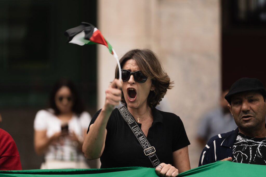 Woman passionately protesting in Rabat, Morocco, waving flag and shouting slogans.