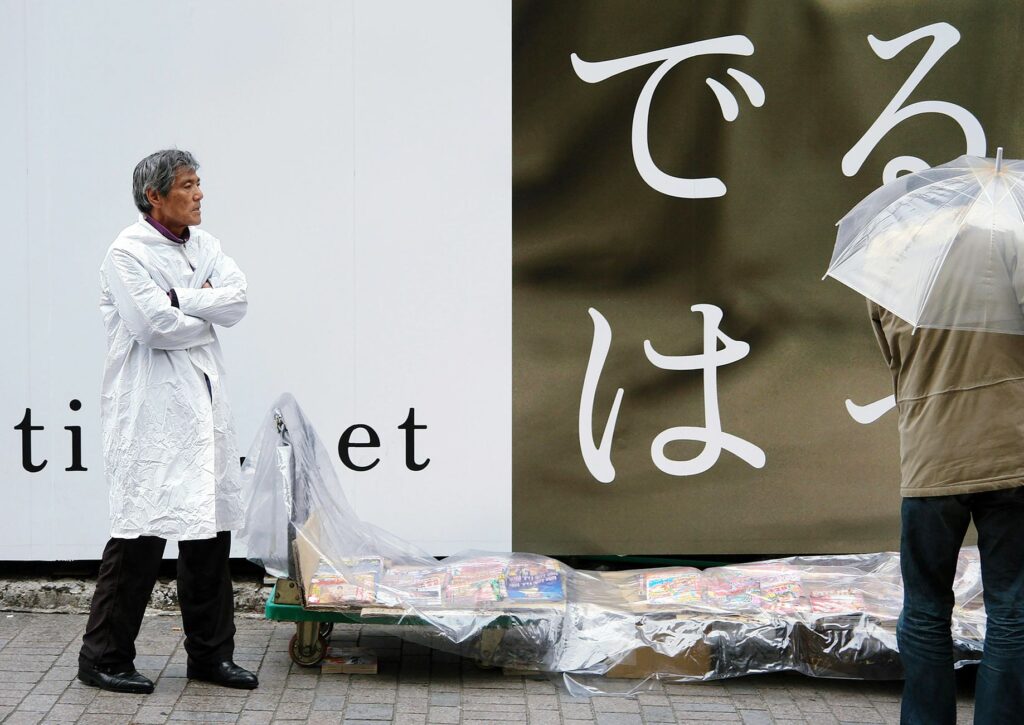 Street vendor and passerby with umbrella under rain in Tokyo, contrasting Japanese urban scene.