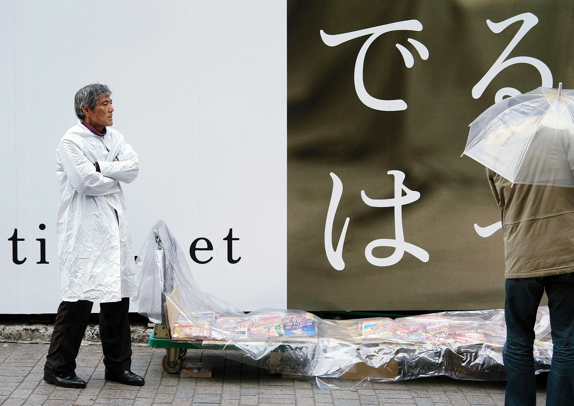 Street vendor and passerby with umbrella under rain in Tokyo, contrasting Japanese urban scene.