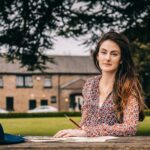 A brunette woman with long hair paints outdoors in a Dublin park, exuding creativity.