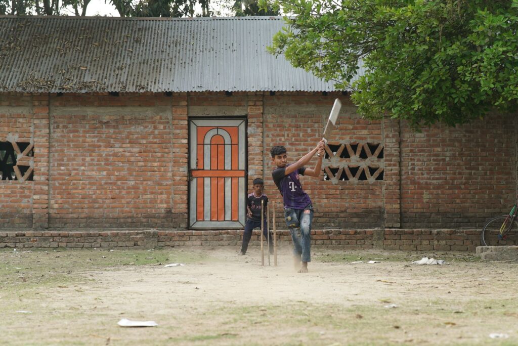 Two boys enjoying a casual game of cricket in a village setting.