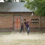 Two boys enjoying a casual game of cricket in a village setting.