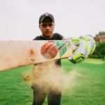 Closeup of cricket bat and ball hit by sportsman wearing sportswear and gloves on blurred background