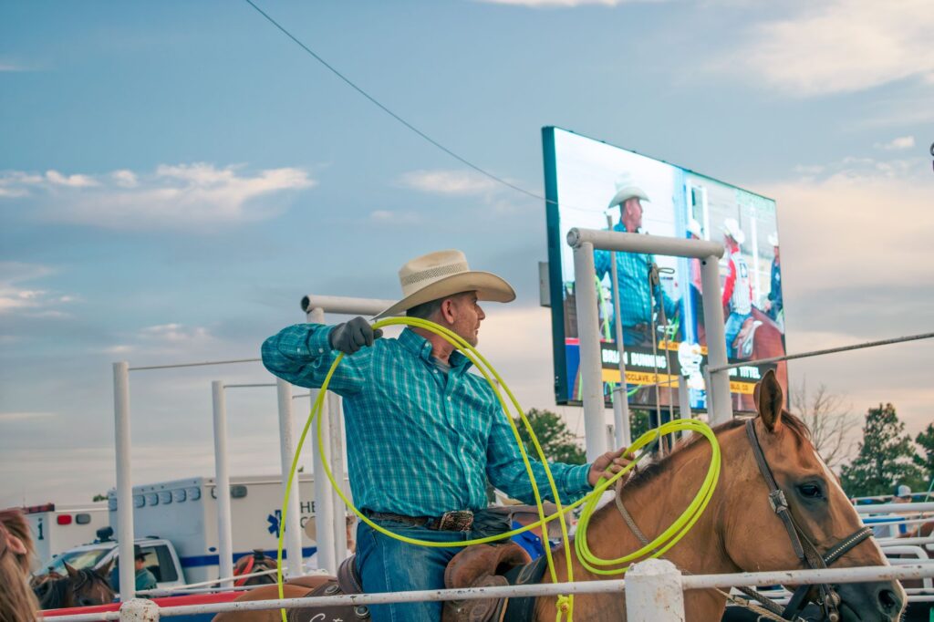 Cowboy in hat skillfully handles lasso during rodeo on horseback outdoors.