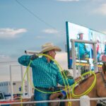 Cowboy in hat skillfully handles lasso during rodeo on horseback outdoors.