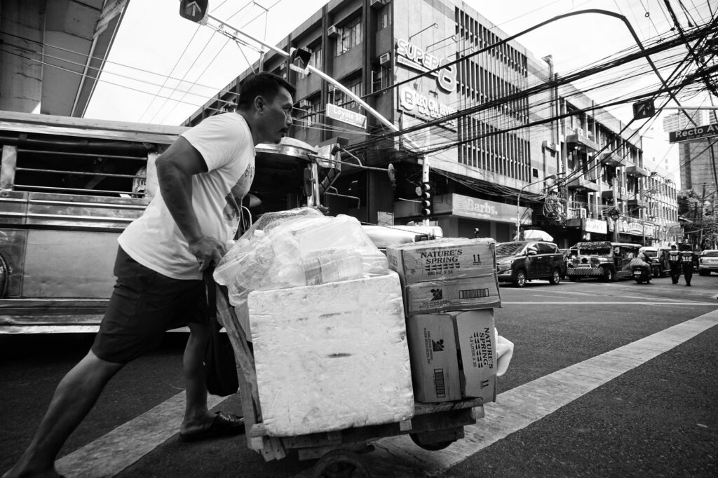 Black and white image of a street vendor pushing a cart in bustling Manila.