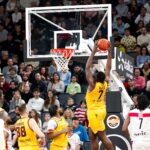 A player jumps to score during a thrilling basketball game with a full crowd.