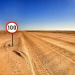 Open desert road with a speed limit sign showing 100 under clear sky.
