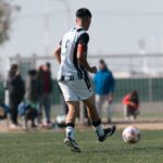 Young soccer player dribbles on field during a bright day match with spectators.