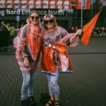 Two joyful soccer fans in raincoats and flags at a stadium entrance, enjoying a vibrant event.