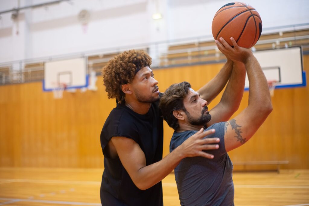 Two men practicing basketball indoors, focusing on improving shooting skills.