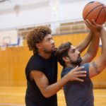 Two men practicing basketball indoors, focusing on improving shooting skills.