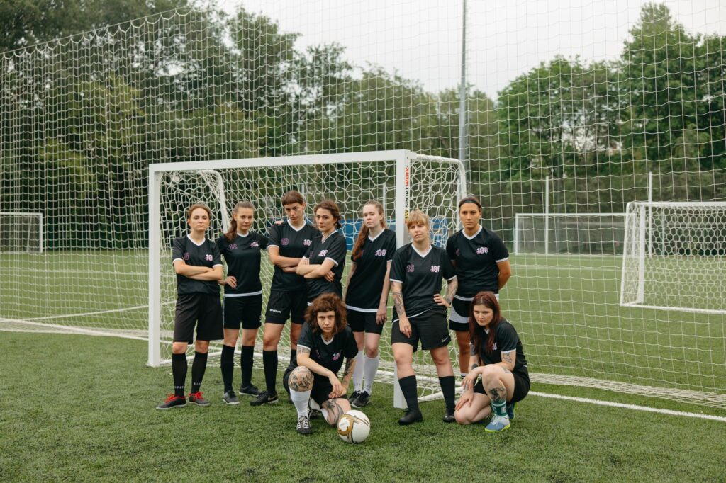 A diverse group of women soccer players pose confidently on a green soccer field.