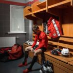 Hockey player in red sportswear sitting on a wooden bench in a locker room, preparing for a game.