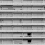 A black and white view of a symmetrical high-rise apartment building with closed shutters.