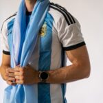 Close-up of a person wearing an Argentina jersey holding a flag, indoors.