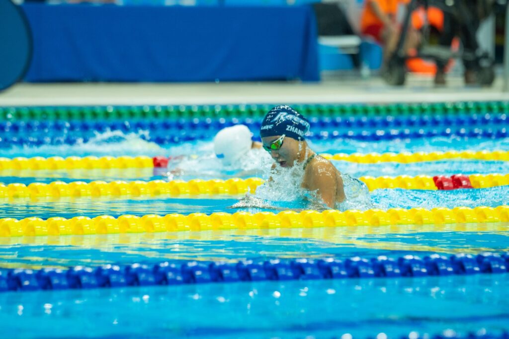 Swimmers compete in a vibrant indoor pool setting during a race with colorful lane markers.