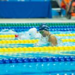 Swimmers compete in a vibrant indoor pool setting during a race with colorful lane markers.