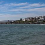 Picturesque coastline with ocean waves and coastal houses under a clear blue sky.
