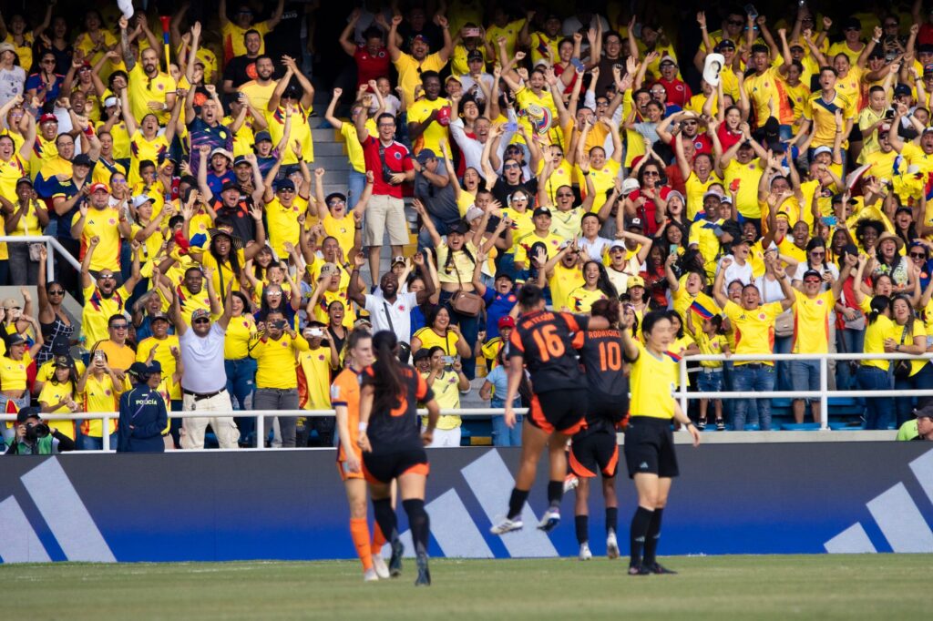 Energetic crowd of Colombian football fans cheering at a match in a vibrant stadium.