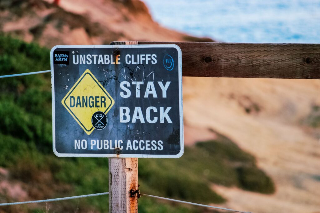 Warning sign indicating danger due to unstable cliffs, advises staying back. Outdoors setting.