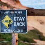 Warning sign indicating danger due to unstable cliffs, advises staying back. Outdoors setting.