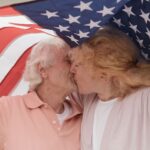 Senior couple sharing a kiss under an American flag, symbolizing love and patriotism.