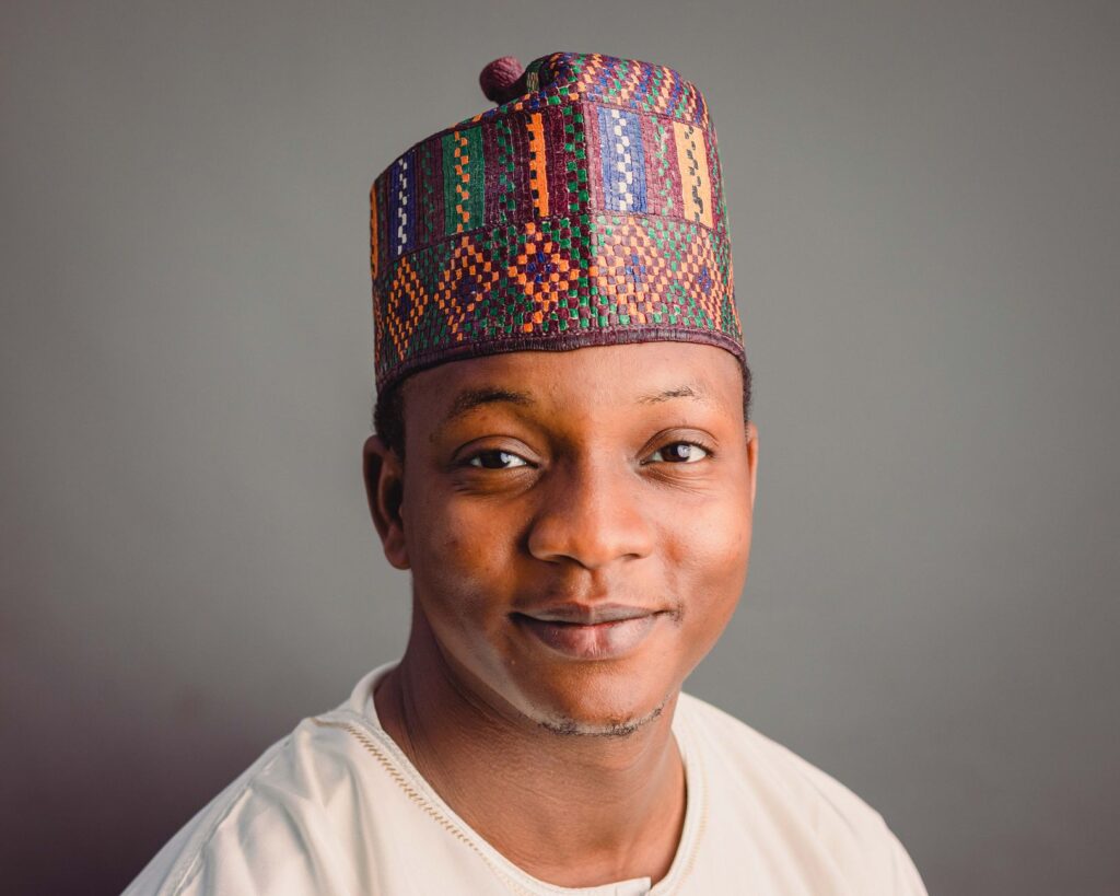 Portrait of a smiling Nigerian man wearing a colorful traditional hat.