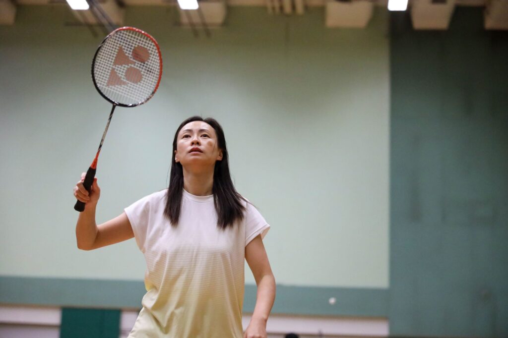 Woman playing badminton indoors, showcasing focus and sportswear.