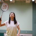 Woman playing badminton indoors, showcasing focus and sportswear.