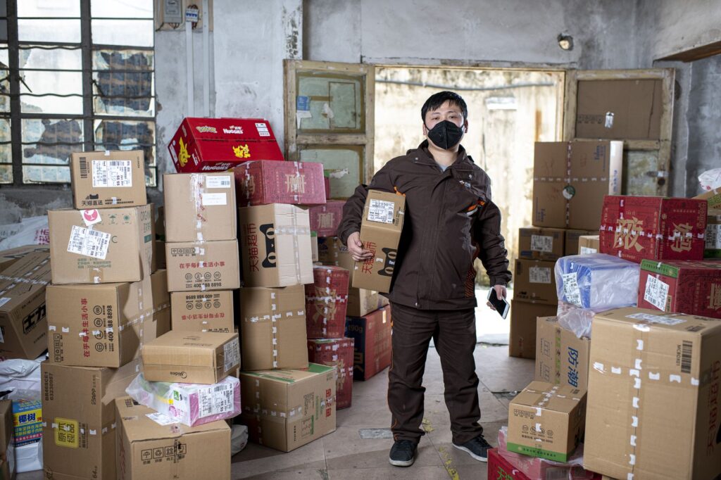 Delivery worker holding packages in a Wuhan warehouse, wearing a face mask.