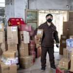 Delivery worker holding packages in a Wuhan warehouse, wearing a face mask.