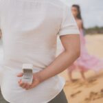A man hides an engagement ring behind his back, preparing to propose on a beach in Phu Quoc.